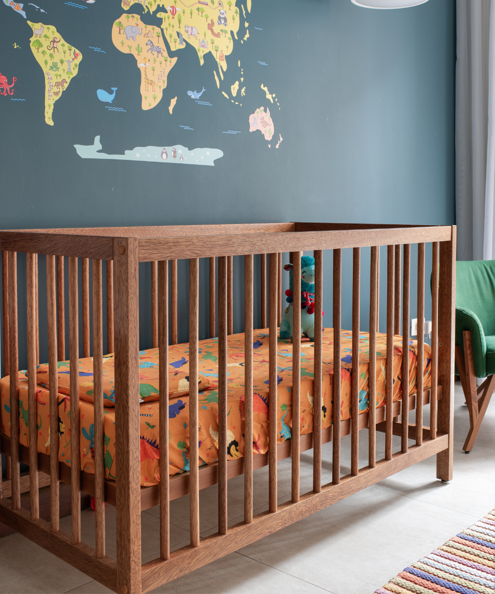 Berço de madeira com roupa de cama laranja e estampa de animais. Mapa-múndi decorativo na parede azul.