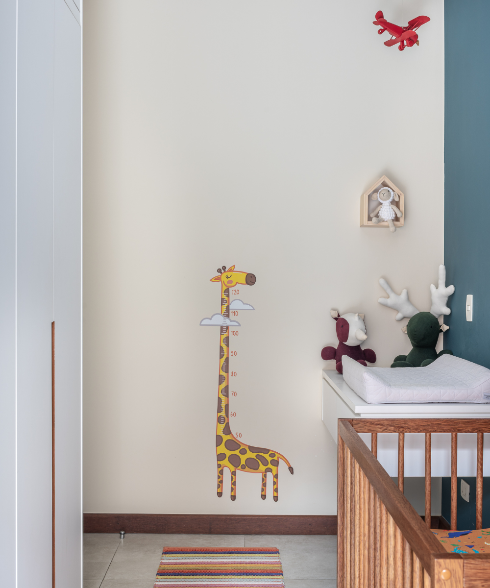 Quarto infantil com girafa medidora na parede, aviões e brinquedos decorando.