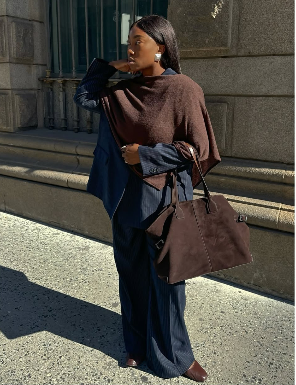 Mulher em traje formal, com casaco e bolsa grandes, simbolizando Power Dressing, em ambiente urbano.