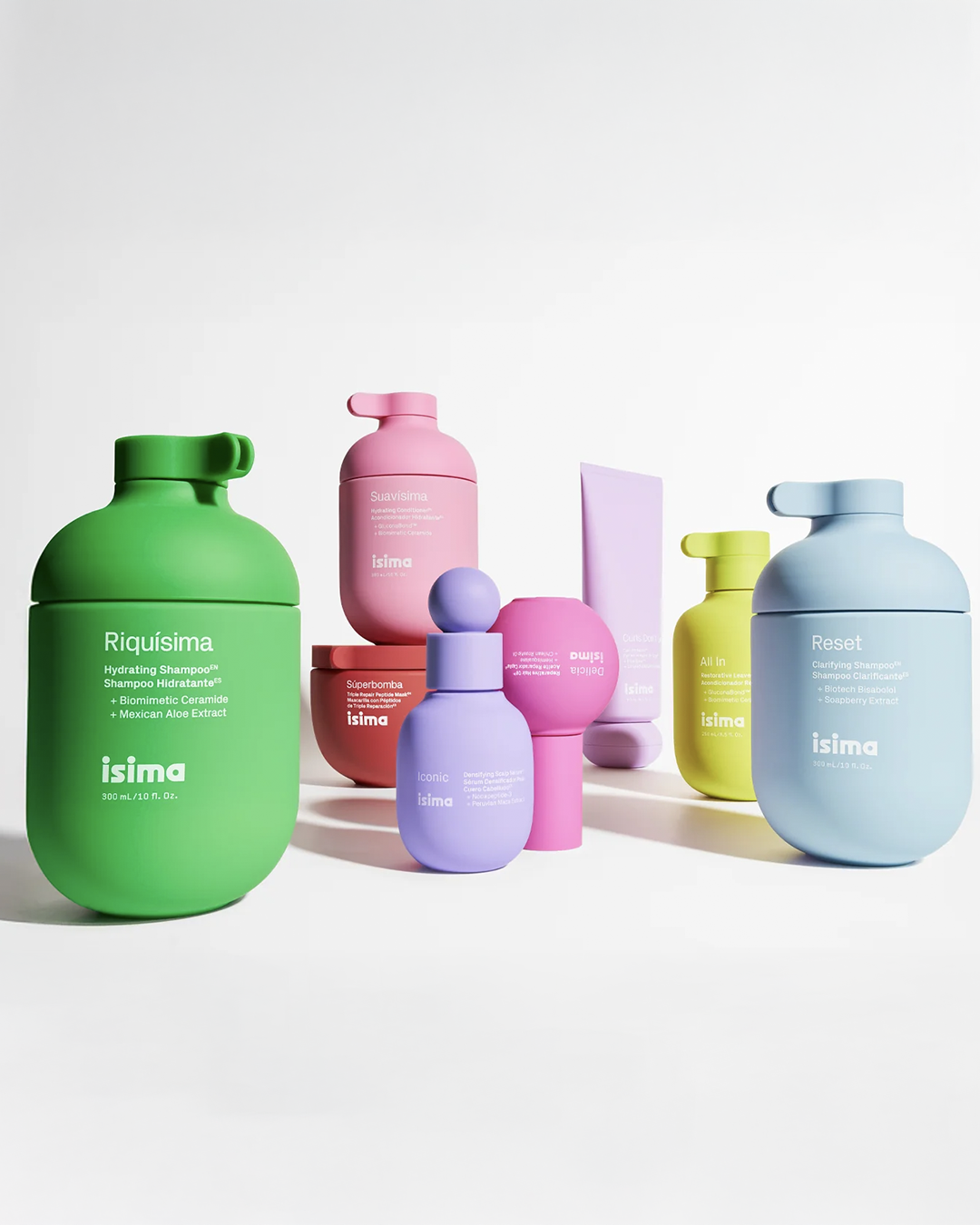 Frascos coloridos de produtos de beleza arranjados sobre superfície branca, incluindo shampoo e hidratantes. Shakira