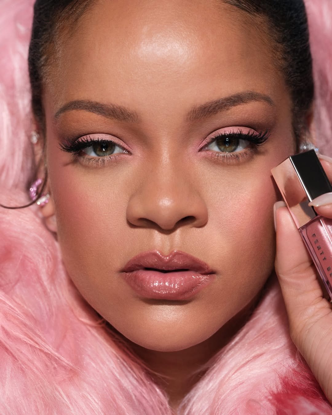 Mulher com maquiagem rosa segura um produto de beleza próximo ao rosto.