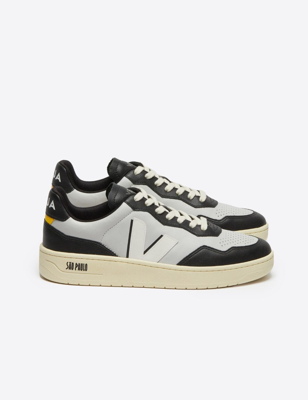 Tênis branco e preto com detalhes em amarelo, design esportivo. Marca VEJA visível na parte traseira.