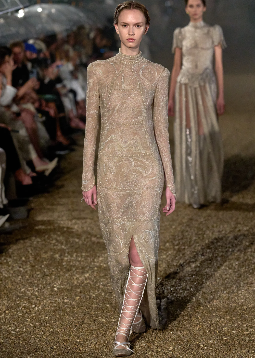 Modelo desfilando em passarela com vestido brilhante e sapatilha de amarração branca.