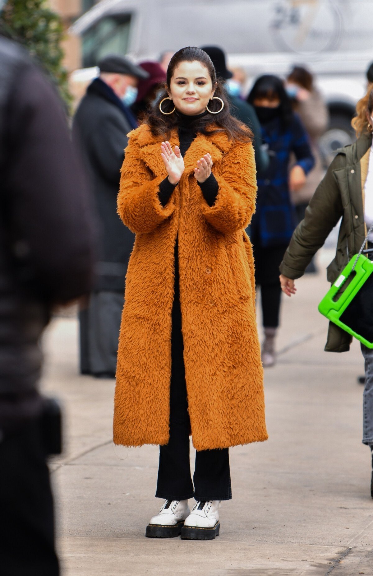 Pessoa usando um casaco teddy marrom claro, sorrindo e aplaudindo na rua.
