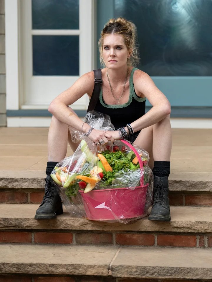 Mulher sentada em degraus com olhar pensativo, segurando cesta de compras cheia de vegetais e frutas. Sereias