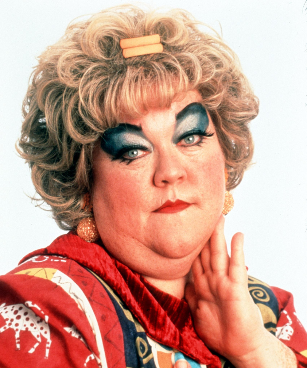 Essa mulher com cabelo cacheado e maquiagem chamativa usa sombra azul nos olhos e batom vermelho.