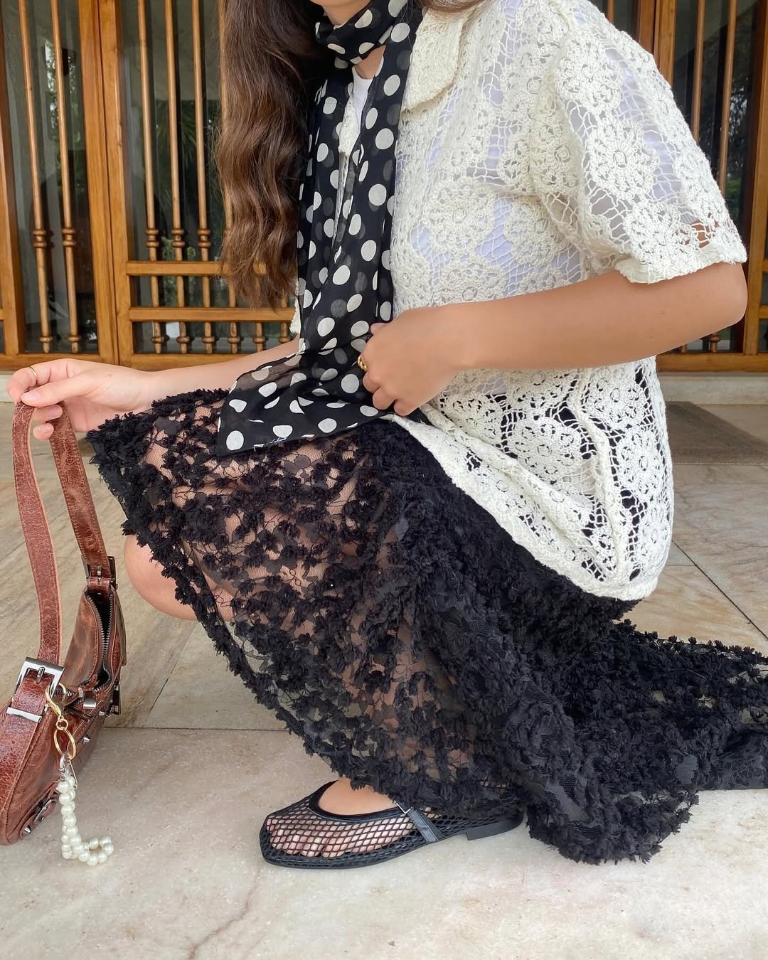 Mulher de vestido rendado e cachecol, usando sapatilha de rede, tendências de sapatilha. Bolsa marrom ao lado.
