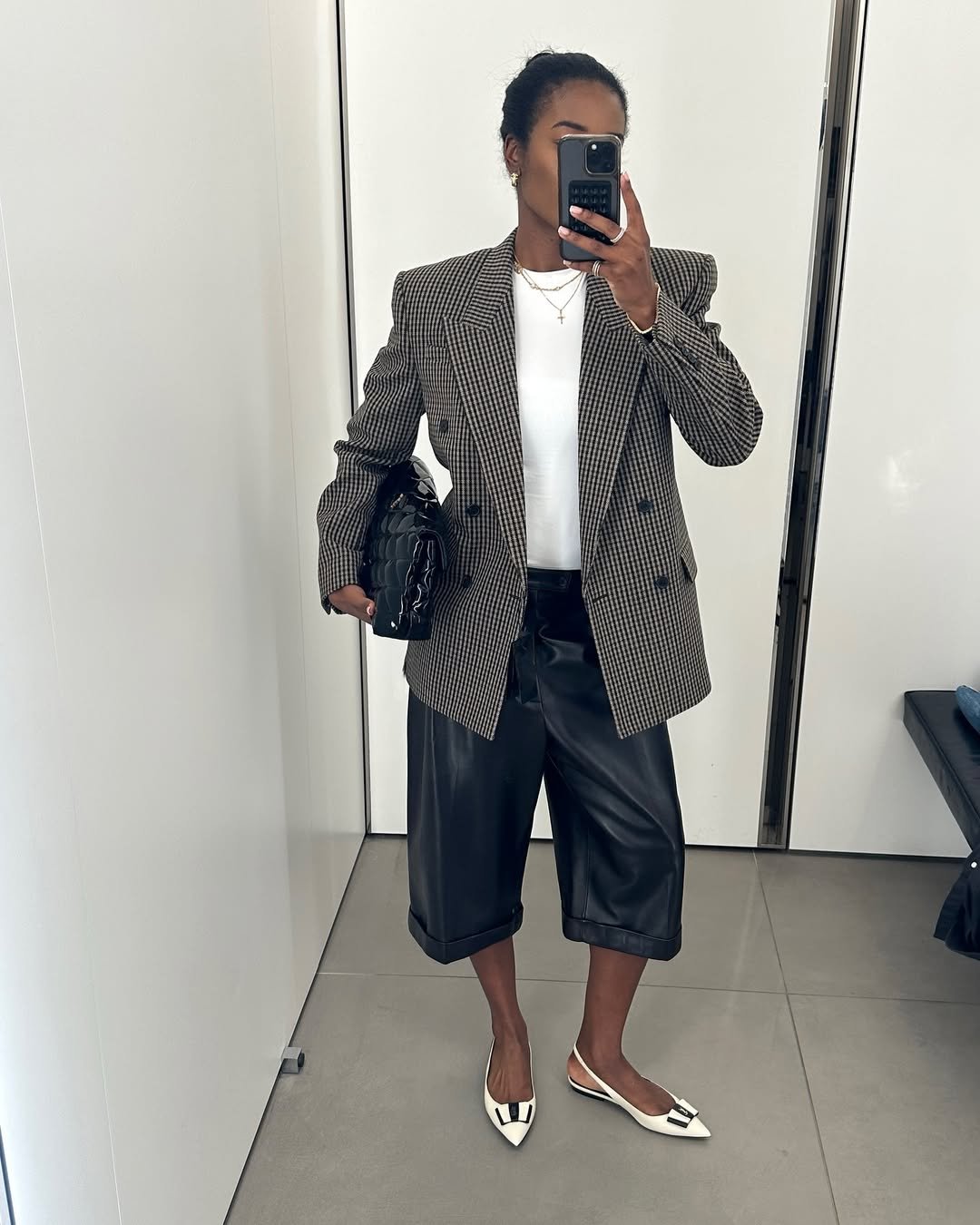 Mulher com blazer xadrez, camisa branca, bermuda preta e sapatilha com detalhe geométrico, refletindo tendências de sapatilha.