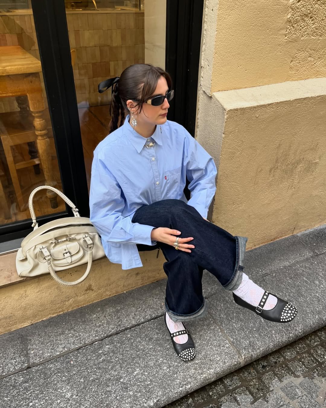 Jovem com camisa azul e óculos escuros usa sapatilhas pretas com detalhes, refletindo tendências de sapatilha.