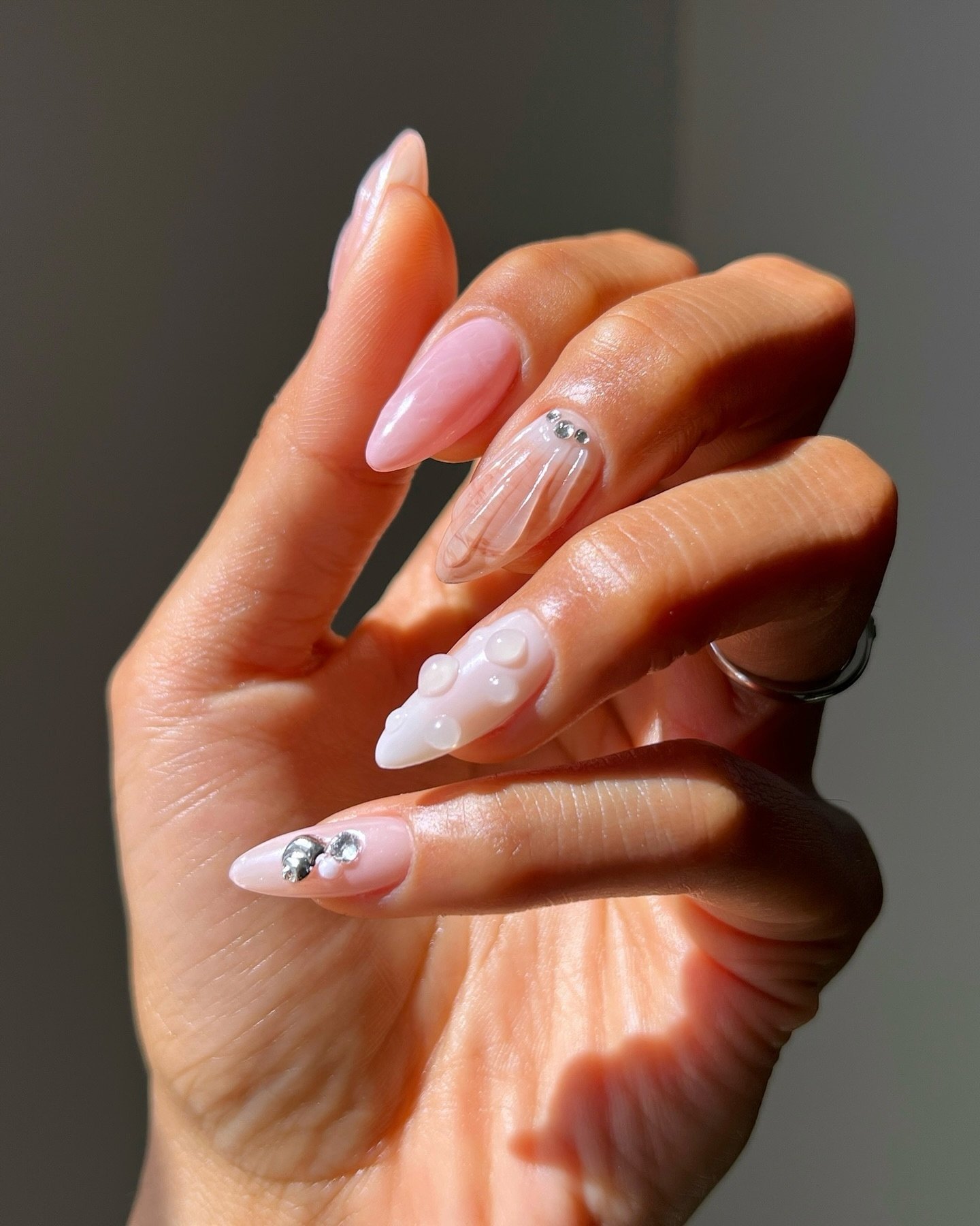 Unhas decoradas coreanas com design transparente, pérolas e pequenos strass brilhantes.