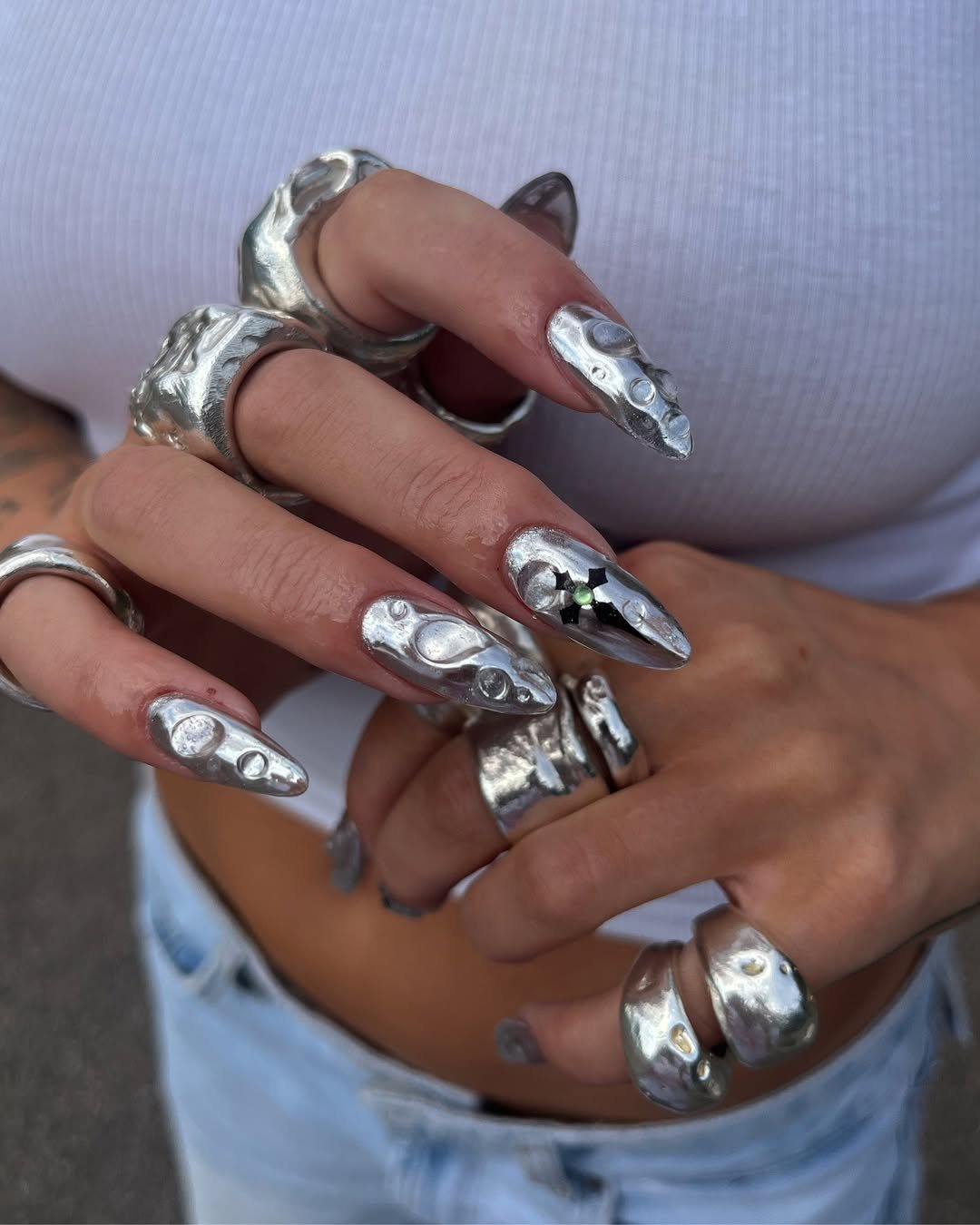 Unhas prateadas decoradas com textura em relevo e anéis chamativos, estilo moderno coreano.