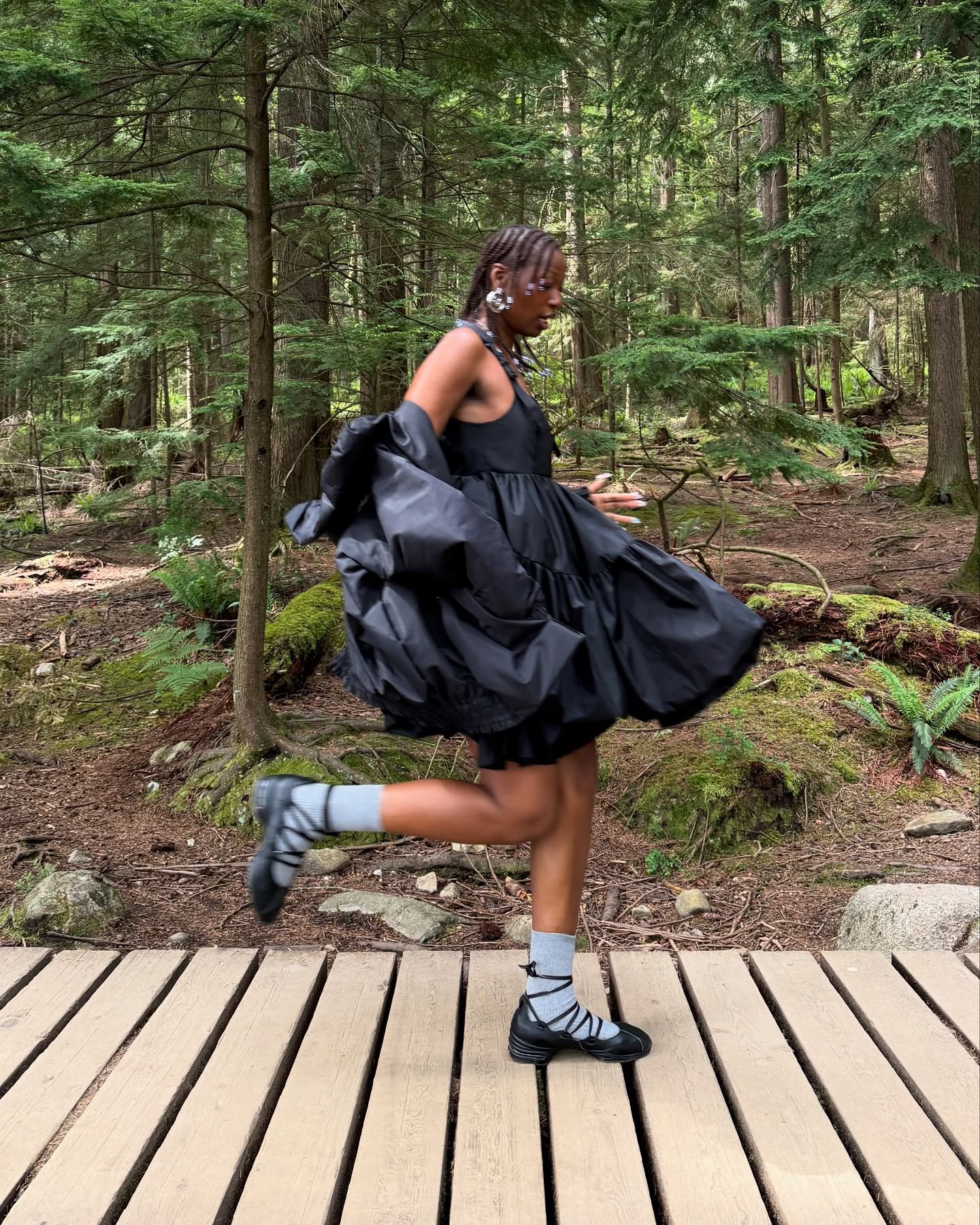 Pessoa usando vestido preto e calçando sapatilha sneakerina corre em passarela de madeira na floresta.