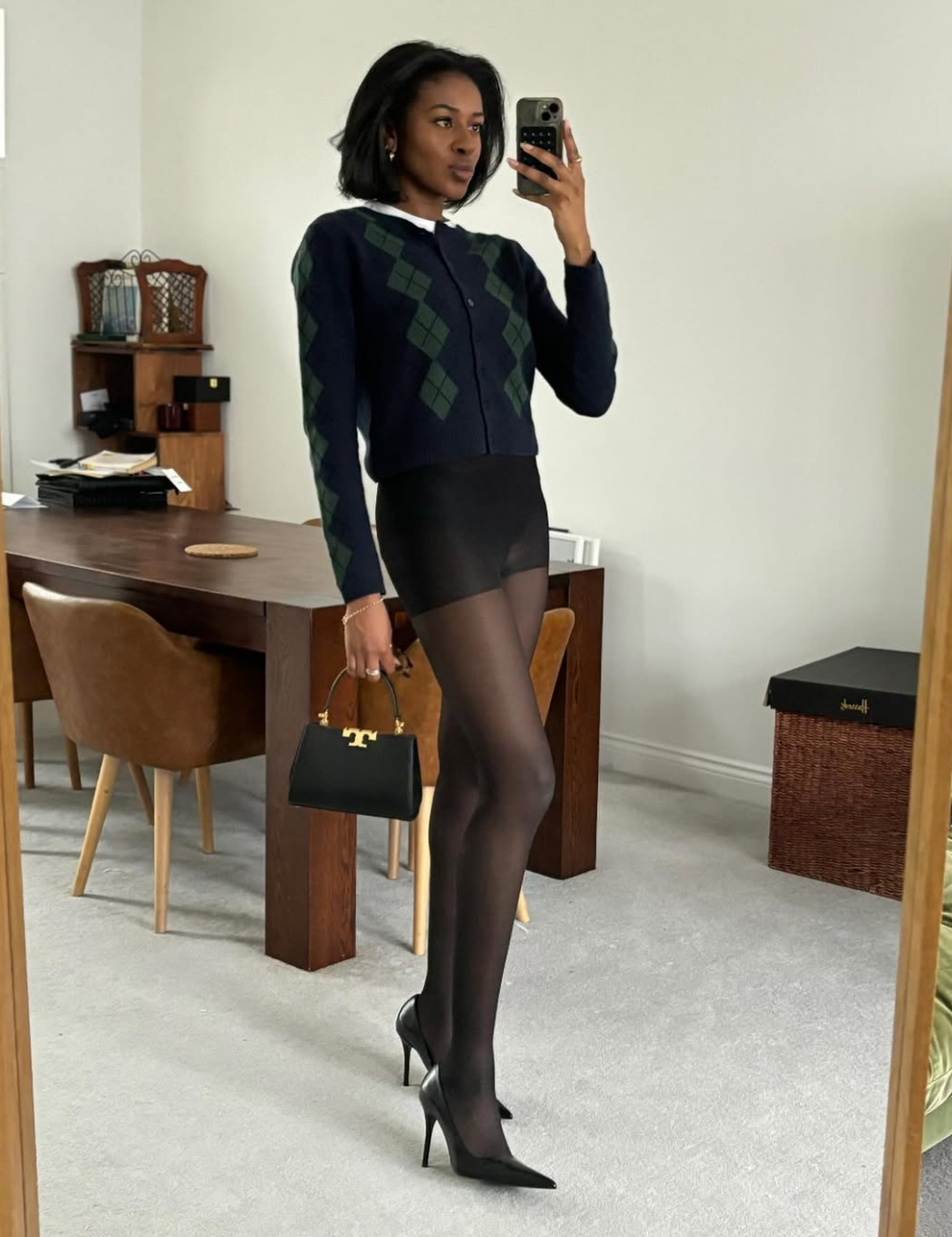 Pessoa com meia-calça preta e salto alto tira selfie em quarto moderno.