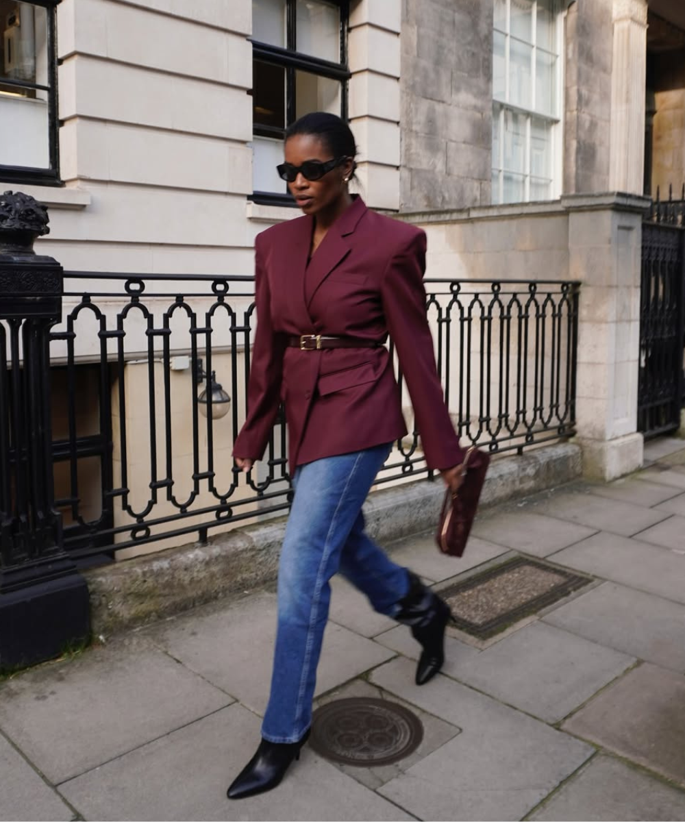 Mulher elegante com casaco vinho e jeans em um passeio urbano, exemplificando estilo casual sofisticado. Usa truques básicos de estilo.
