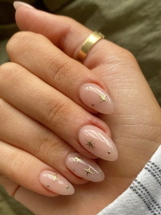 Unha amendoada com esmalte nude decoradas com estrelas douradas.