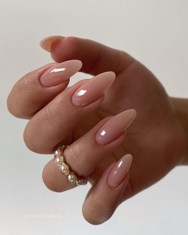 Unha amendoada em tom nude com acabamento brilhante, destacadas por um anel dourado com pérolas.