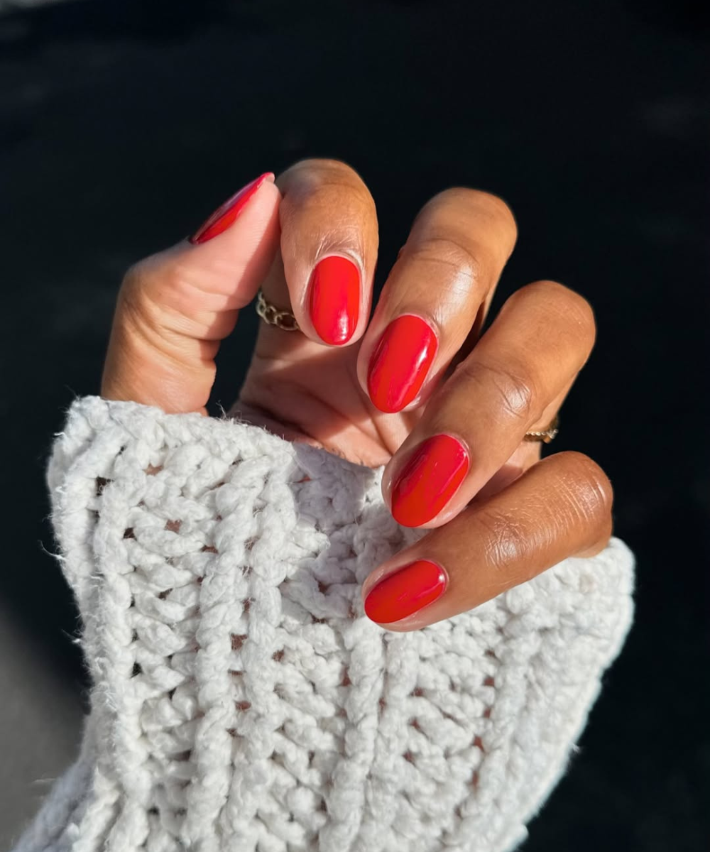 Unhas pintadas de vermelho vibrante com um suéter branco em fundo escuro. Sugestão elegante para noivas.