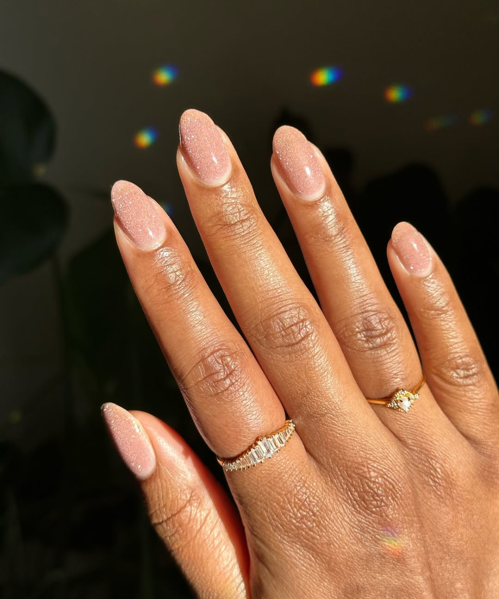 Unhas em tom nude cintilante, ideais para noivas, com anéis dourados delicados.