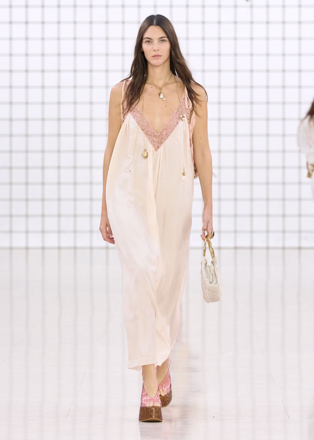 Modelo desfilando em um vestido longo rosa claro com detalhes de renda.