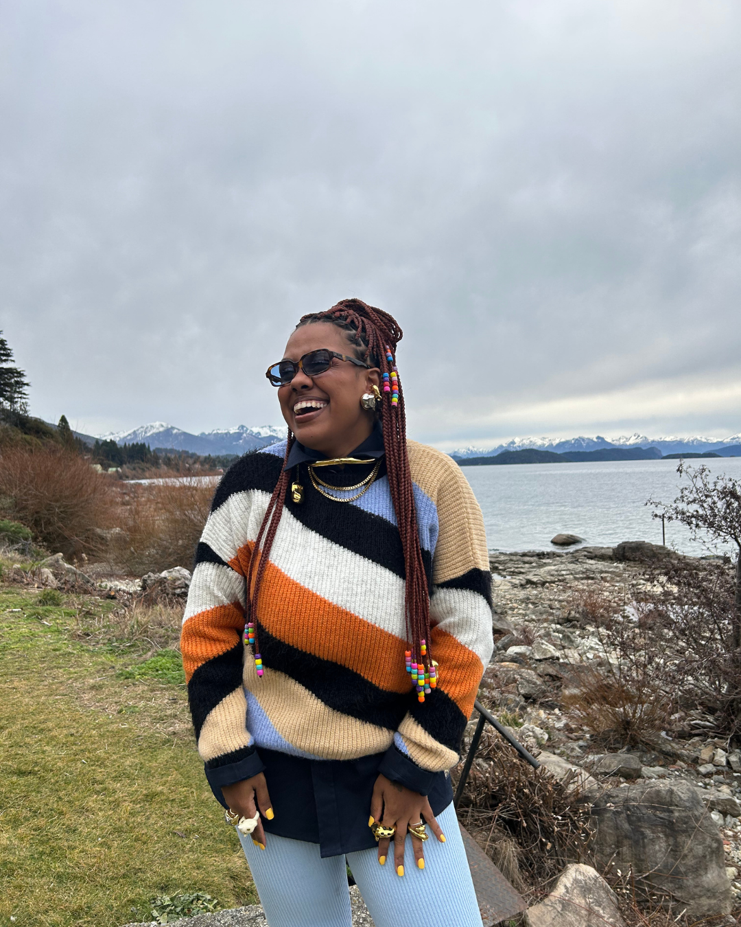 Pessoa sorridente ao ar livre com suéter listrado colorido, uma das tendências de alto inverno. Paisagem montanhosa ao fundo em clima de inverno.