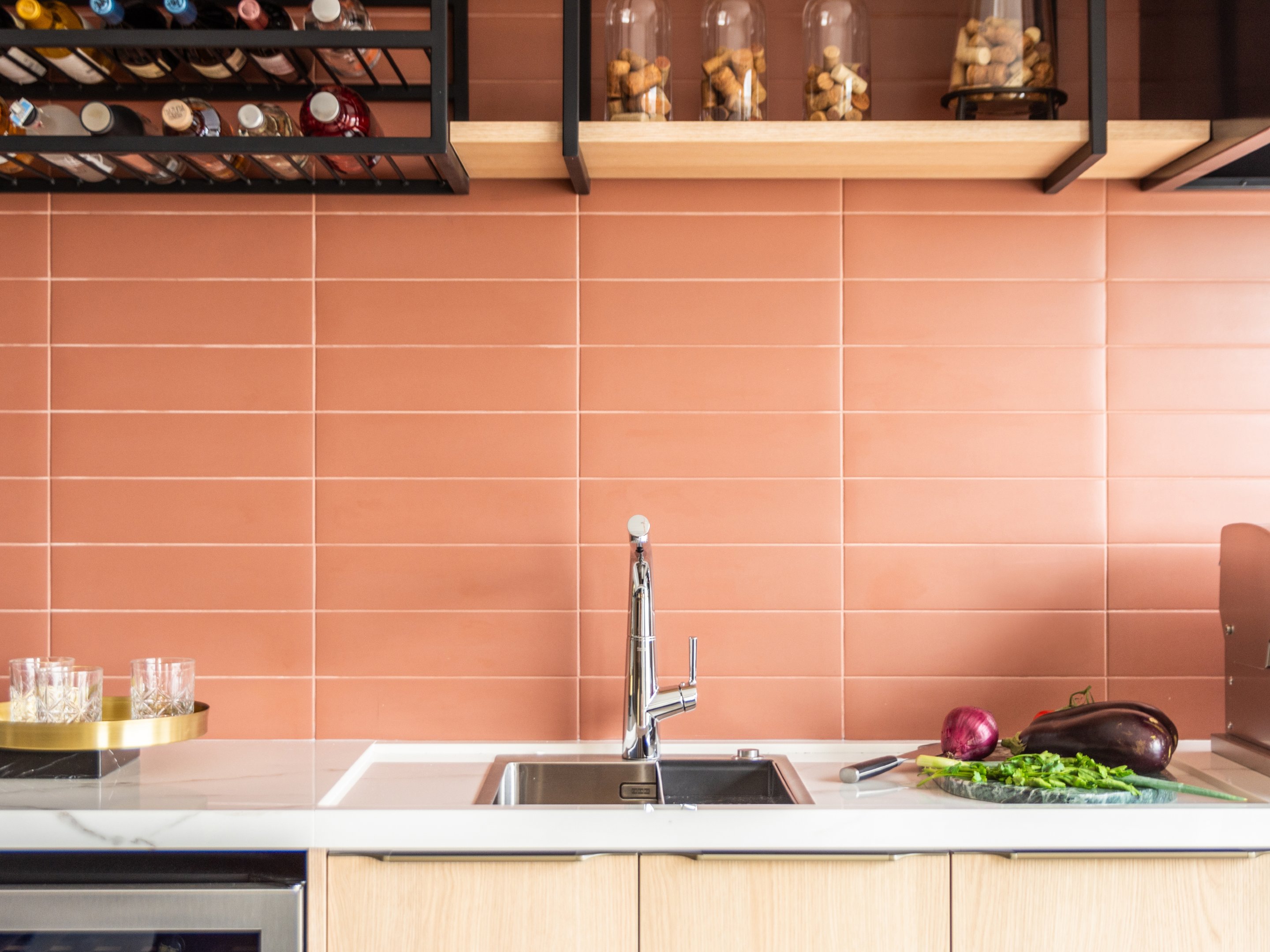 Cuba para cozinha com torneira moderna e ingredientes frescos sobre bancada, fundo de azulejos terracota.