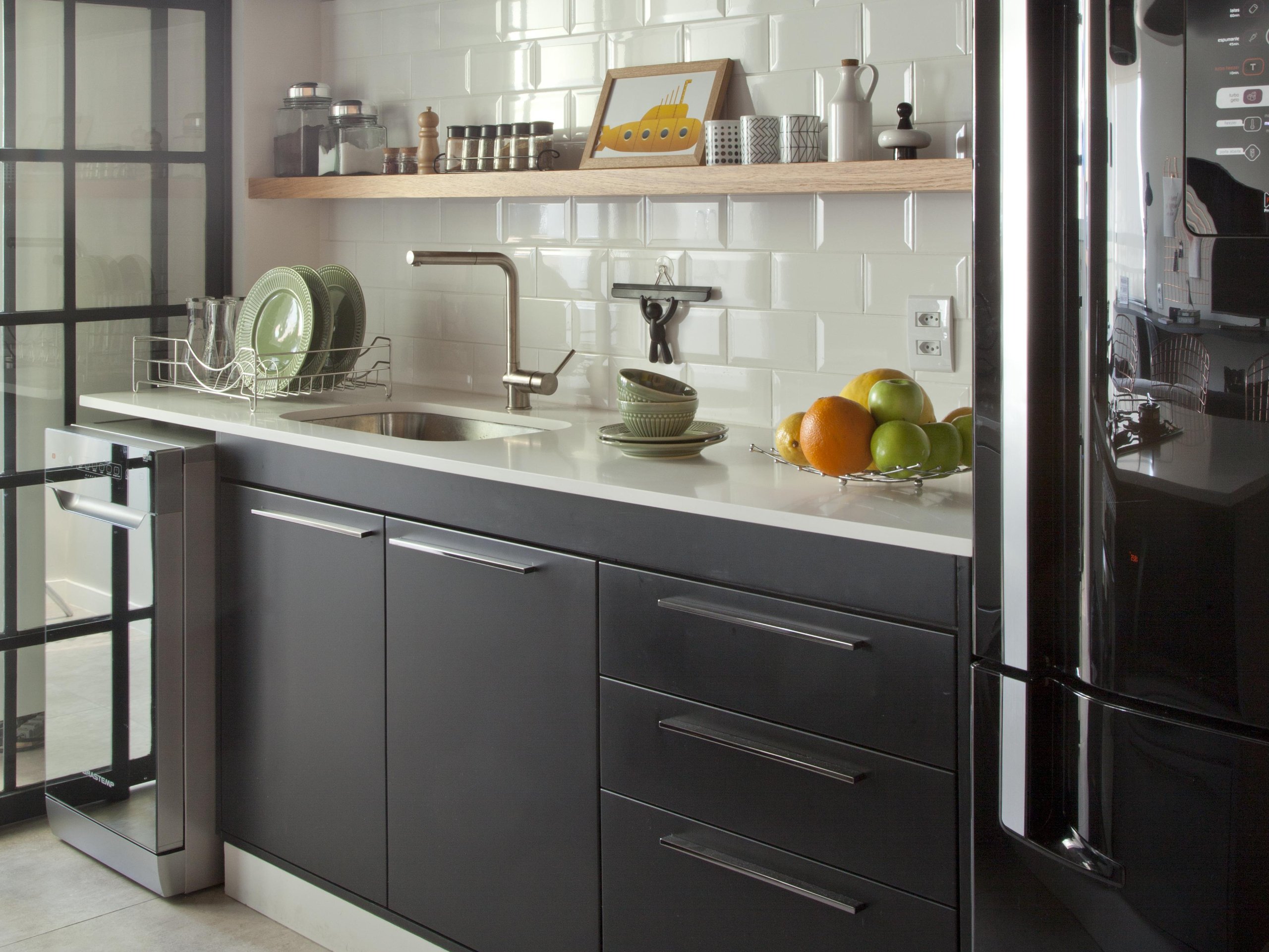 Armário de cozinha moderno com cuba inox, louças verdes, frutas e utensílios na bancada.