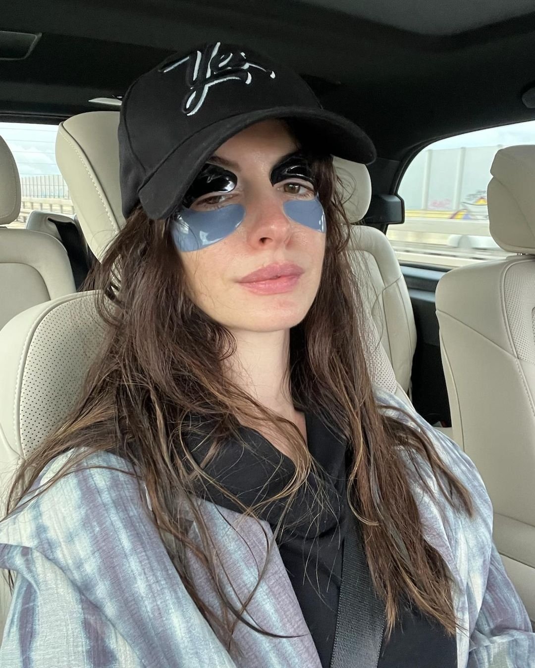 Mulher de boné preto usa eye patches enquanto está sentada em um carro.