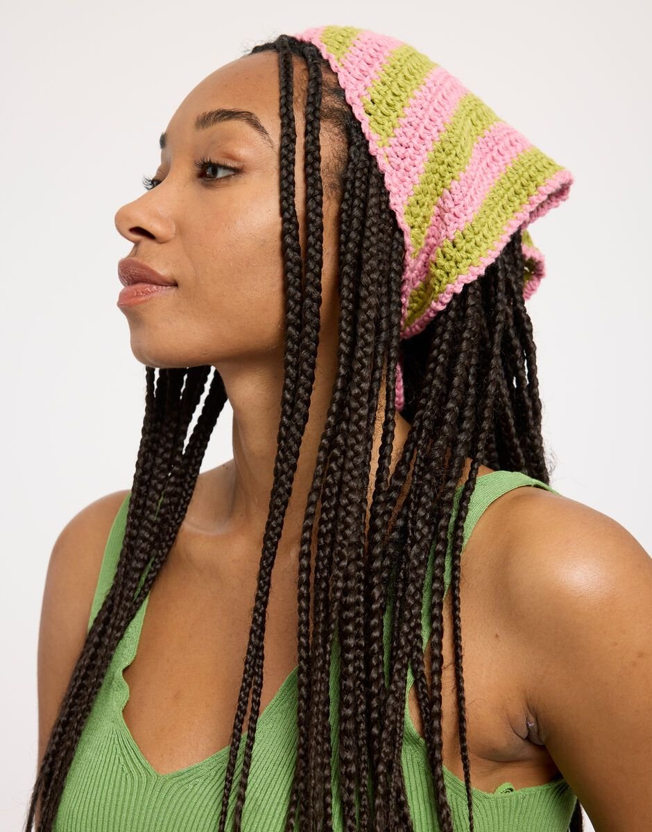 Mulher com cabelo trançado usando bandana de crochê listrada em verde e rosa.