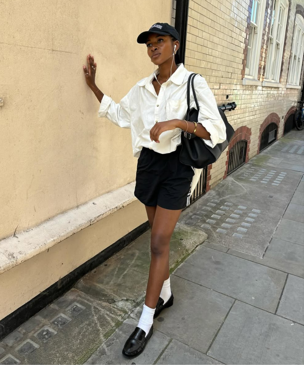 Pessoa usando camisa branca, bermuda esportiva preta e tênis, caminhando ao longo de uma parede.