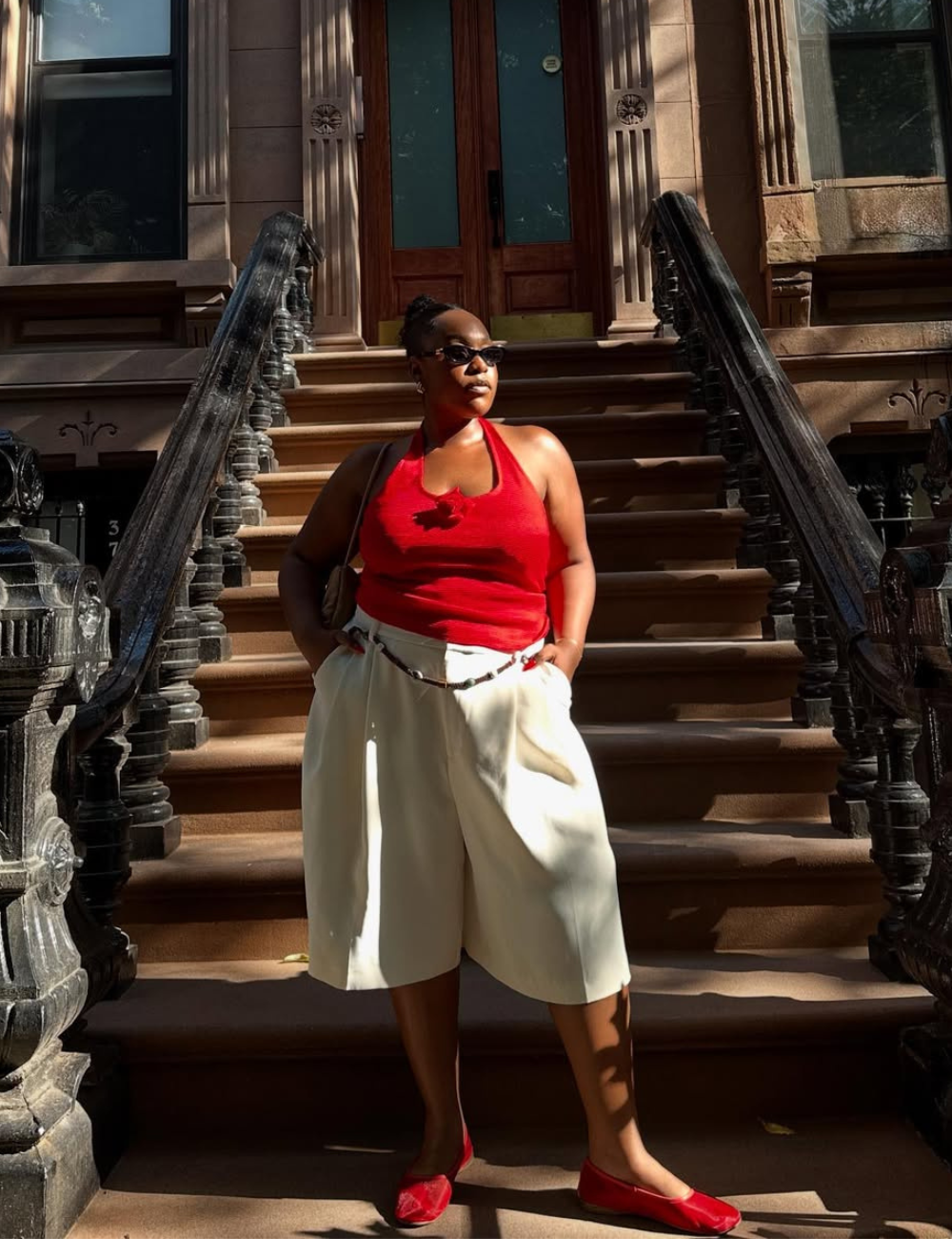 Pessoa usando blusa frente única vermelha e bermuda branca, posando em escadaria urbana.