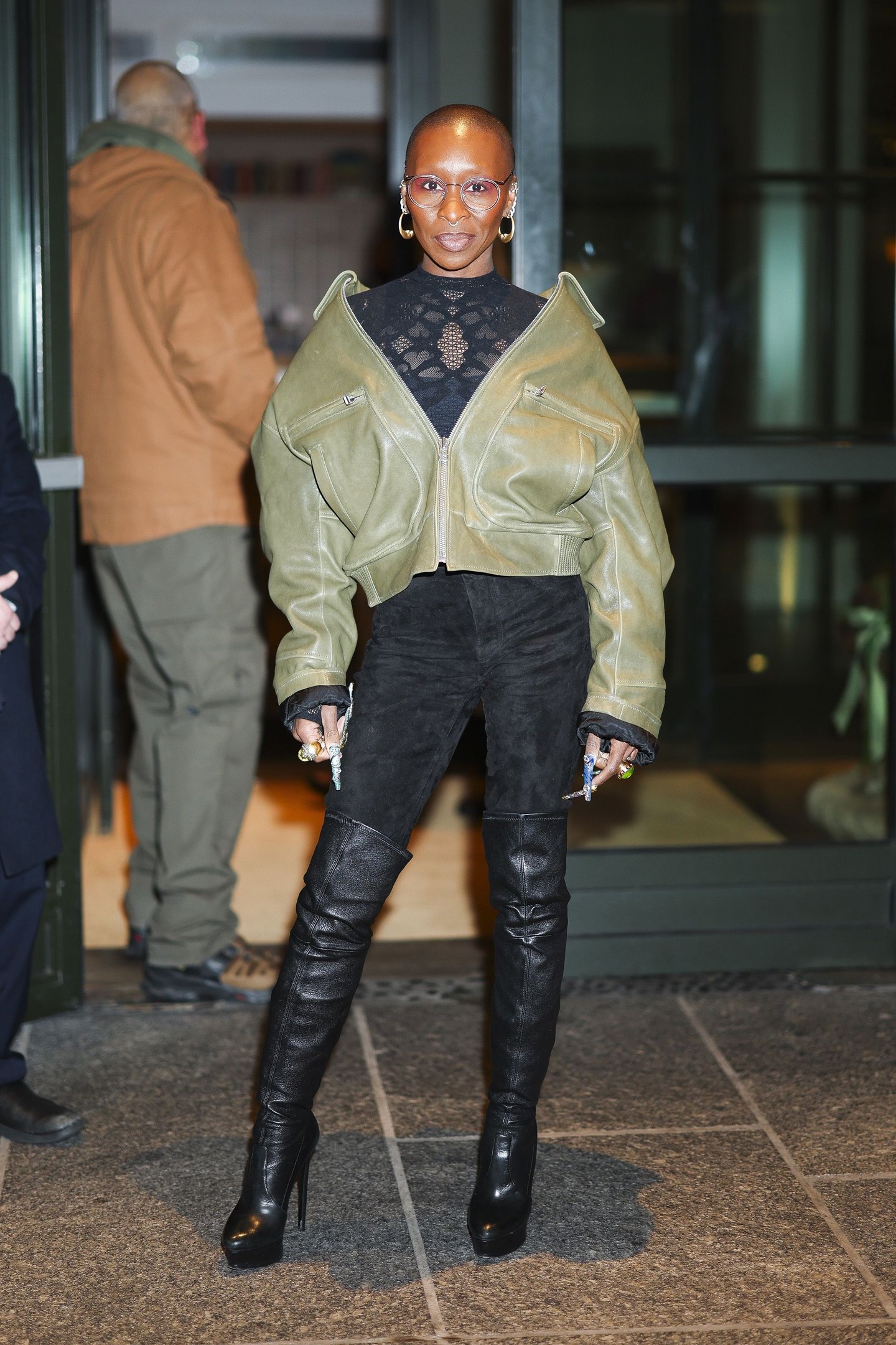 Pessoa usando jaqueta verde e óculos e bota com cano franzido.