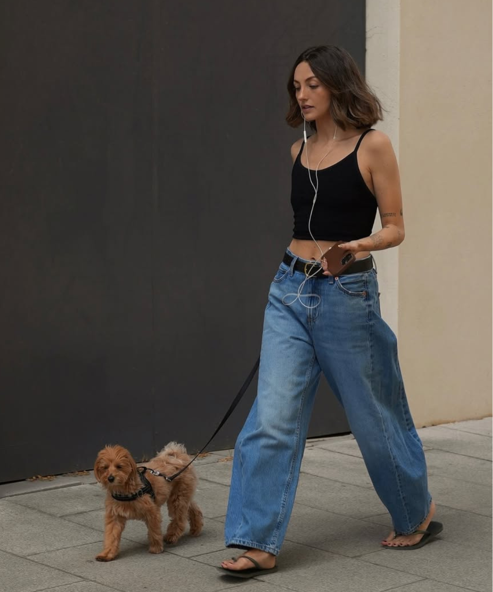 Mulher ouvindo música passeia com cachorro, vestindo calça jeans com chinelo.