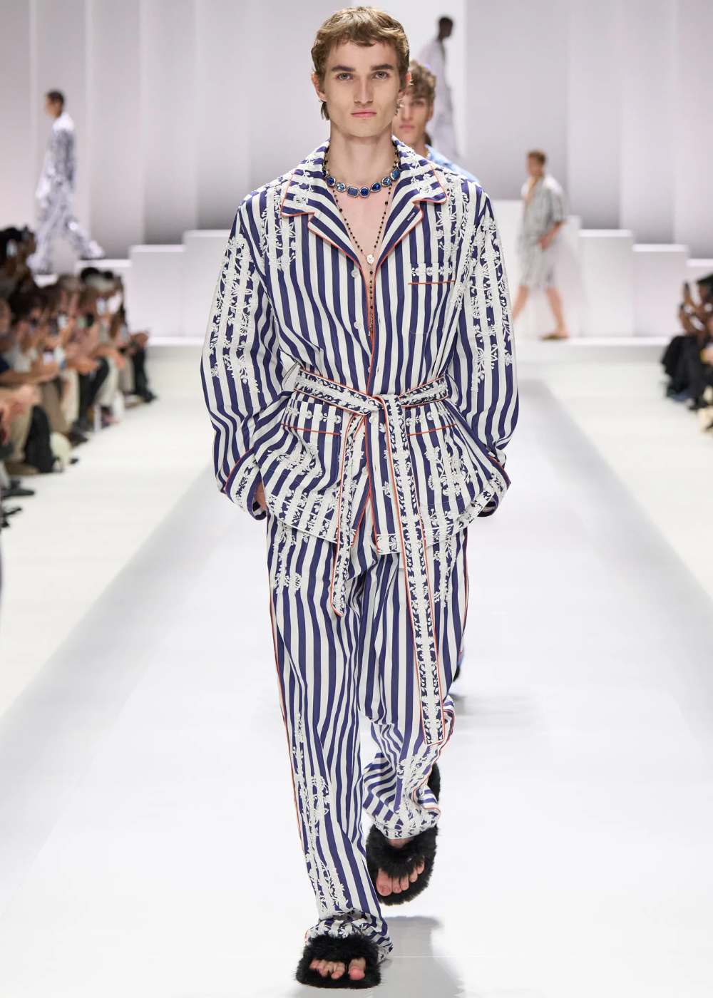 Pessoa desfilando com conjunto listrado azul e branco, usando chinelo peludo.
