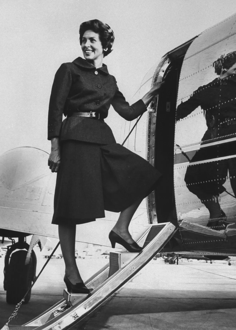Pessoa subindo em avião, vestindo um conjunto elegante com calça culotte preta e sapatos de salto alto.