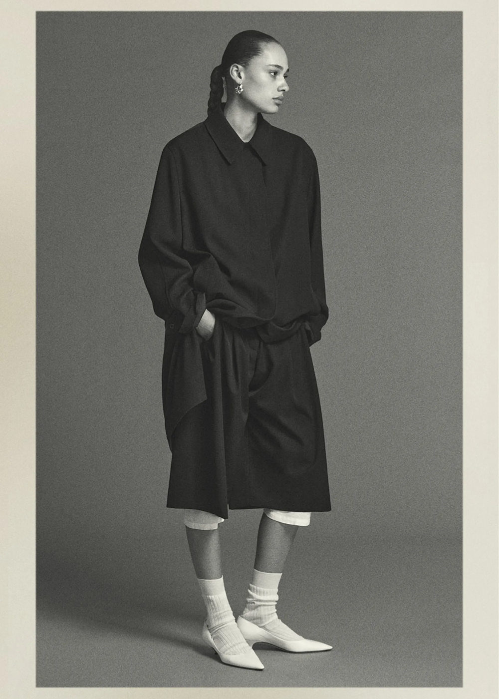Pessoa vestindo calça culotte preta, camisa larga e sapatos de salto, em pose elegante e moderna.
