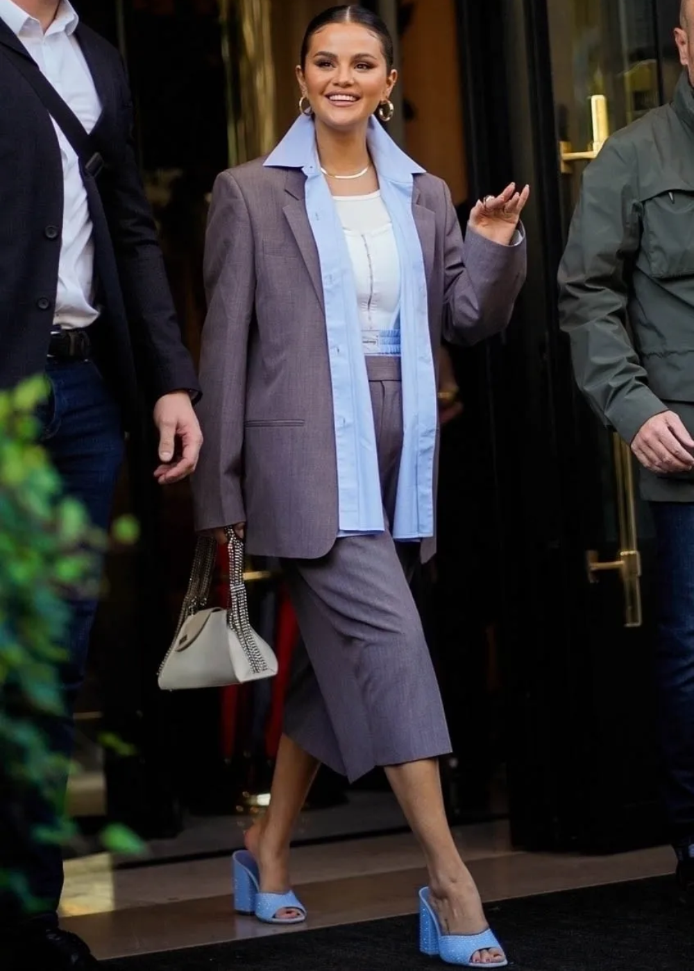 Mulher elegante em calça culotte cinza, blazer e blusa azul, com sandálias de salto azul claro.