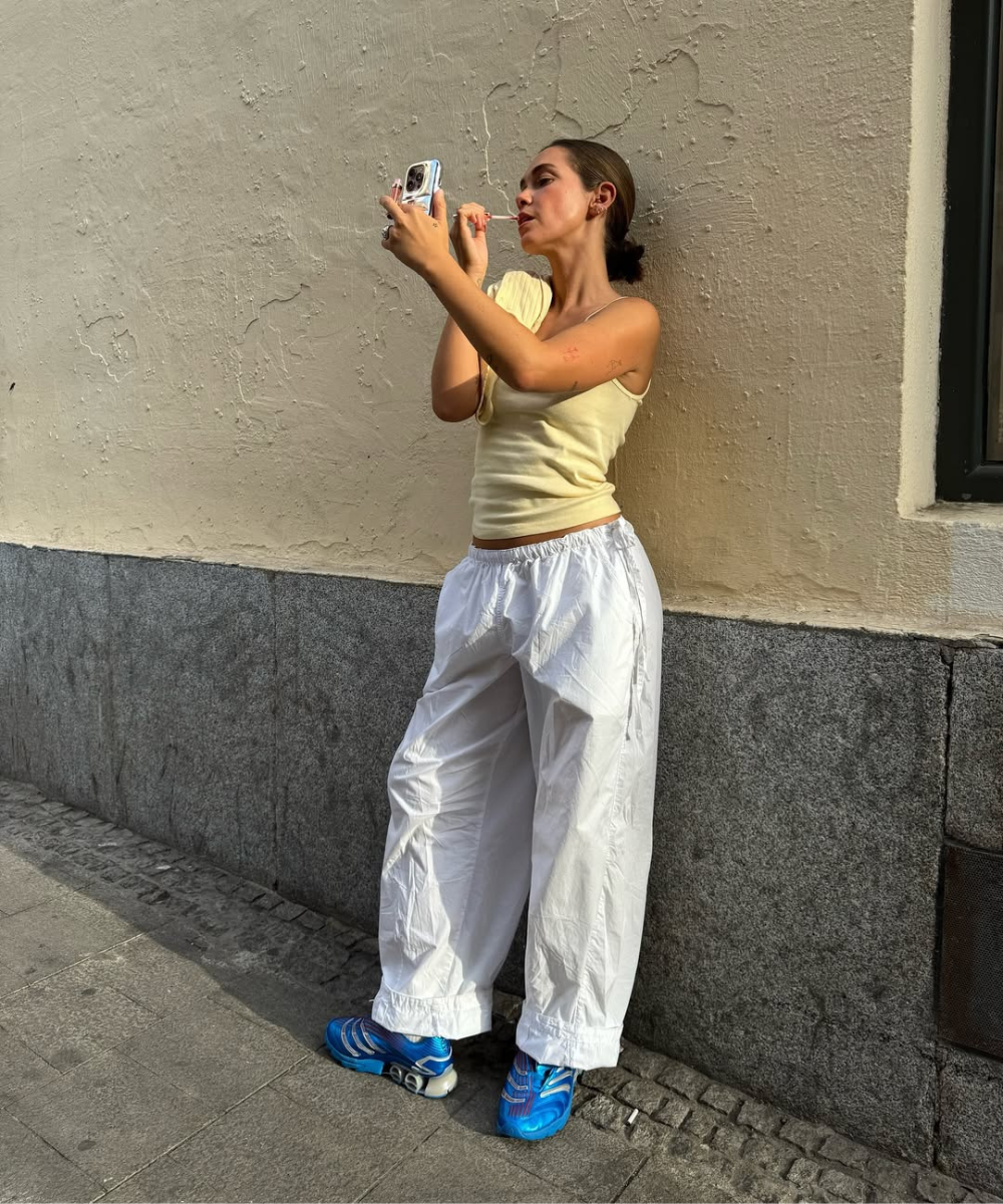 Pessoa vestindo calça de nylon branca e top amarelo, aplicando maquiagem na rua.