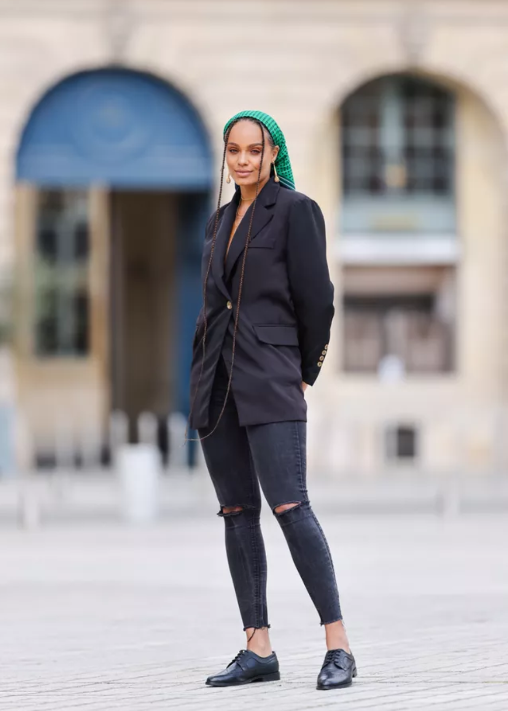 Pessoa usando blazer preto e calças jeans rasgadas, considerada tendência, com lenço verde na cabeça.
