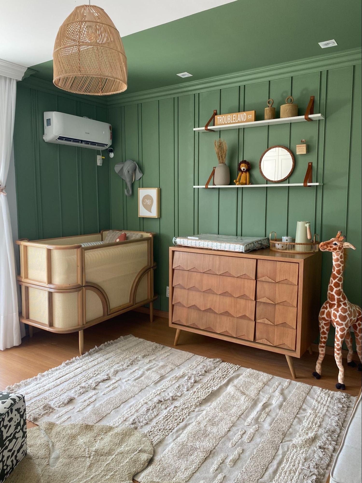 Quarto infantil com paredes verdes, móveis de madeira, decoração de girafa e tapete texturizado. Ambiente aconchegante.