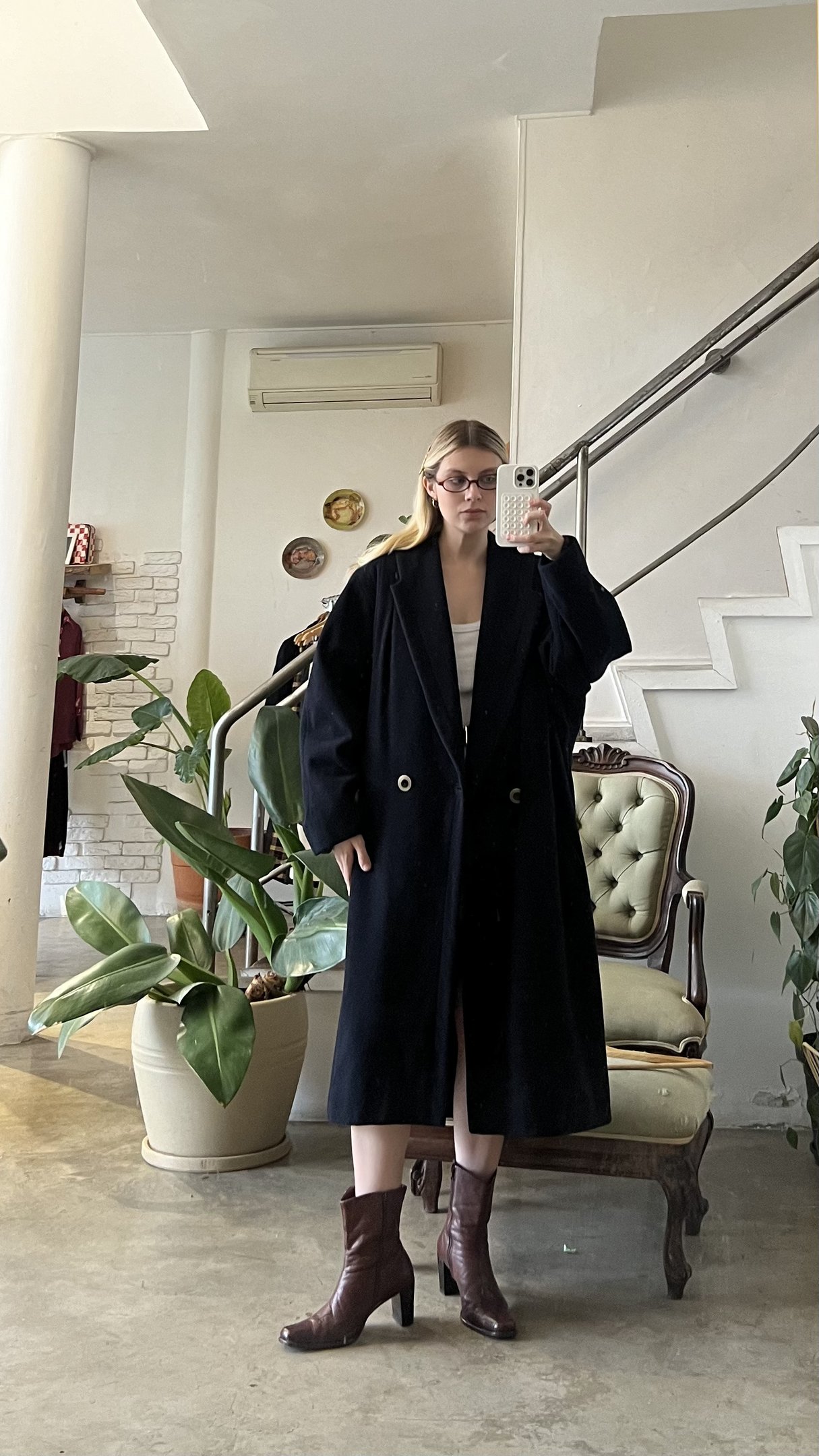 Mulher vestindo casaco longo azul escuro, de frente para espelho em loja.