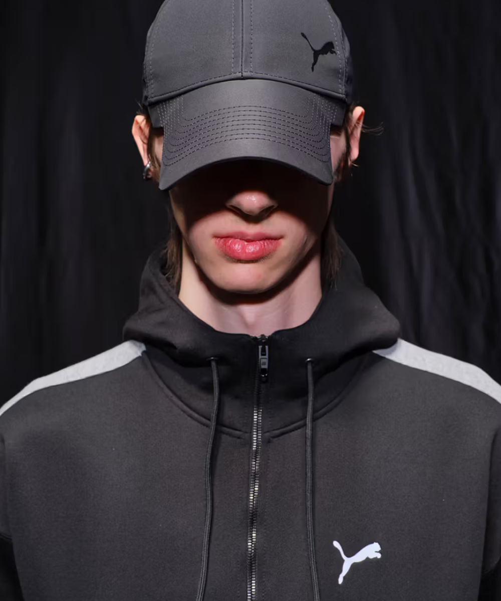 Pessoa vestindo agasalho preto e boné combinando com símbolo de puma, estilo casual e moderno.