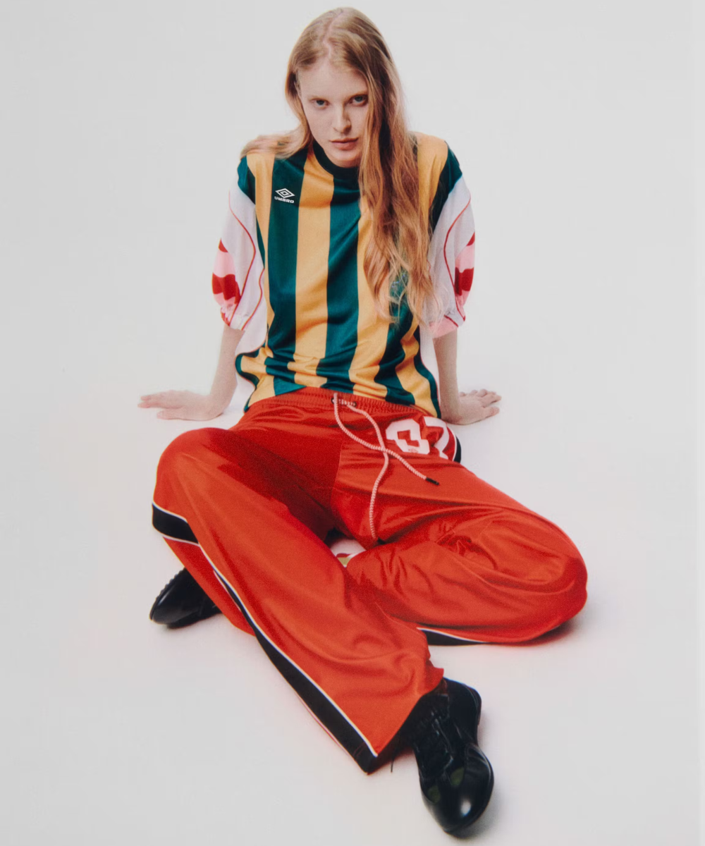Modelo sentada com camisa listrada e calça vermelha, representando collabs de moda.