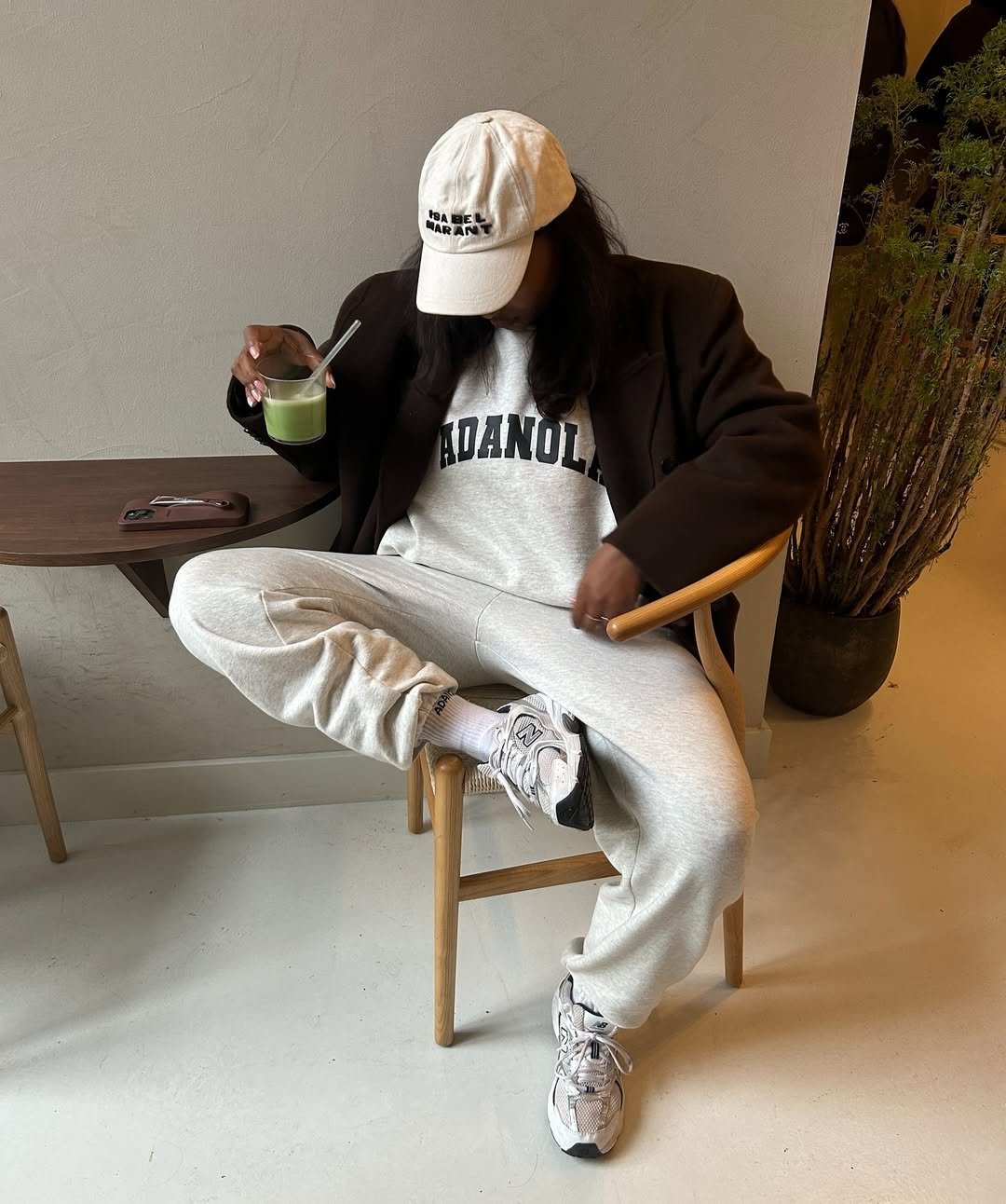 Pessoa vestindo moletom e boné sentada, segura bebida verde. Combos de estilo casual e confortável.