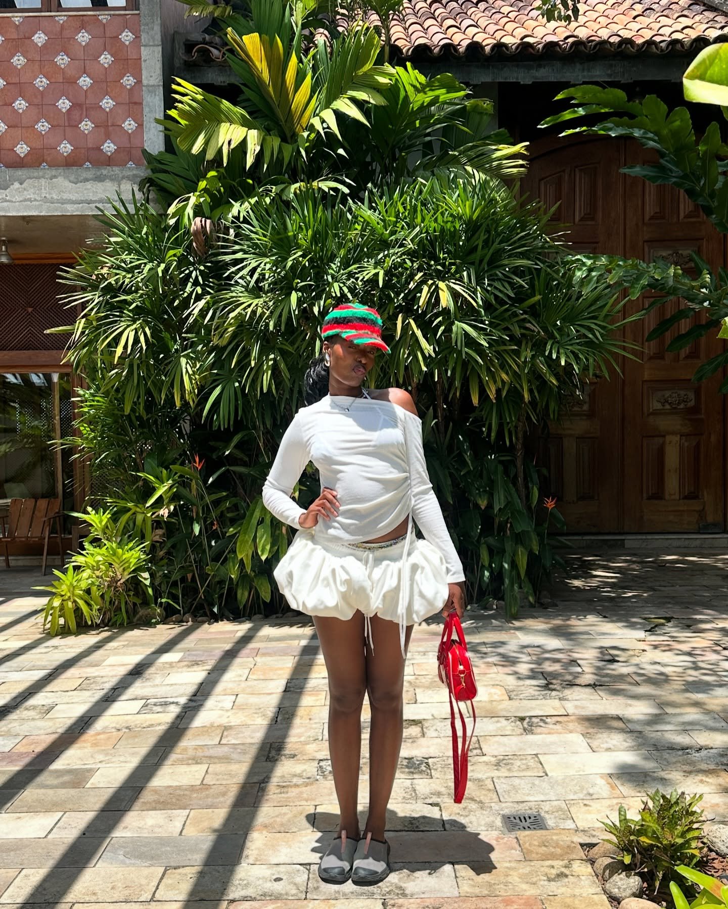 Pessoa com roupa estilosa e casual, composta de blusa branca e saia curta, segura uma bolsa vermelha.