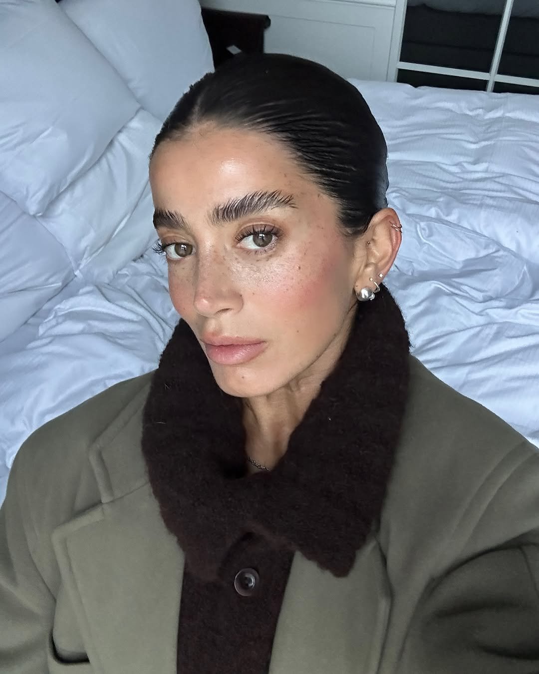 Pessoa com cabelo bem penteado, sobrancelhas definidas e casaco elegante, sugere estilo para entrevista de emprego.