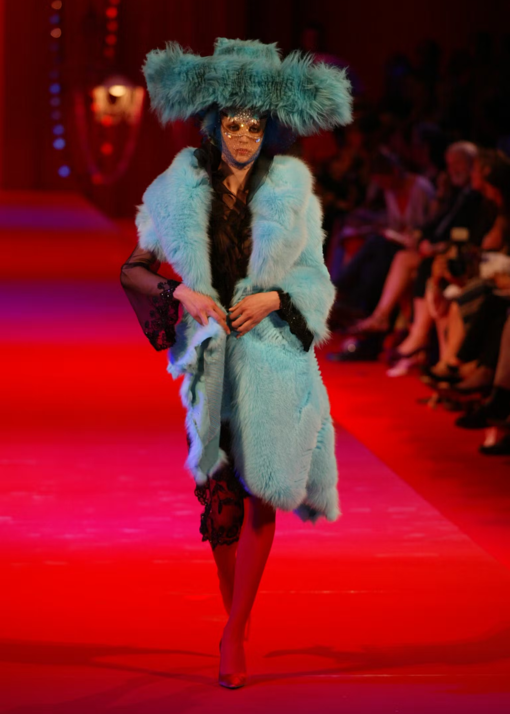 Modelo em passarela com capa azul vibrante e chapéu volumoso, estilo Christian Lacroix.