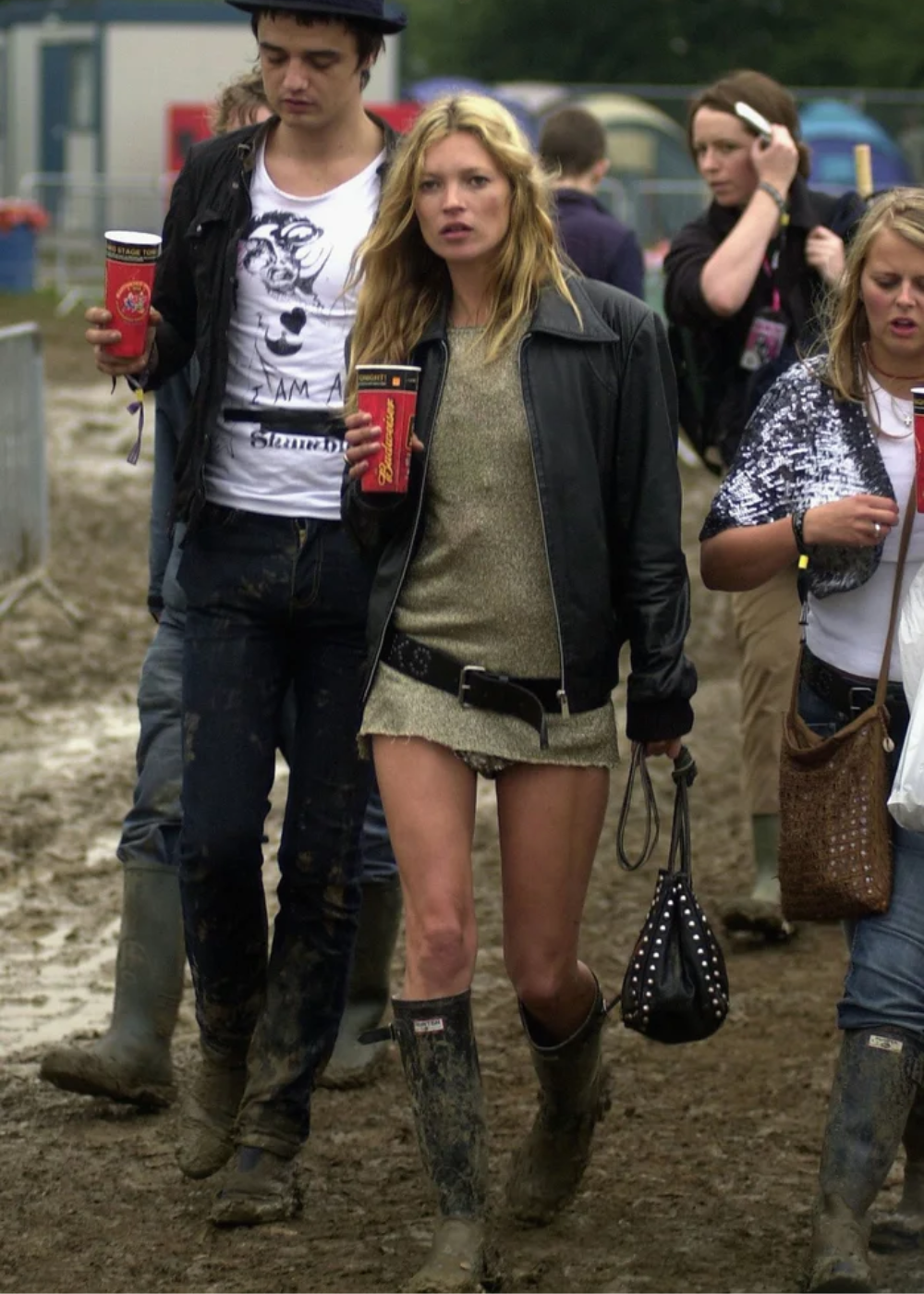 Grupo de pessoas caminhando na lama durante festival ao ar livre. Atmosfera de caos performático.