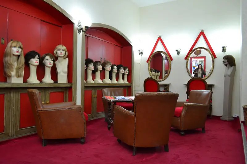 Sala com parede vermelha e espeços, decorada com cadeiras de couro e cabeças de perucas em exposição. Ambiente elegante. Copacabana