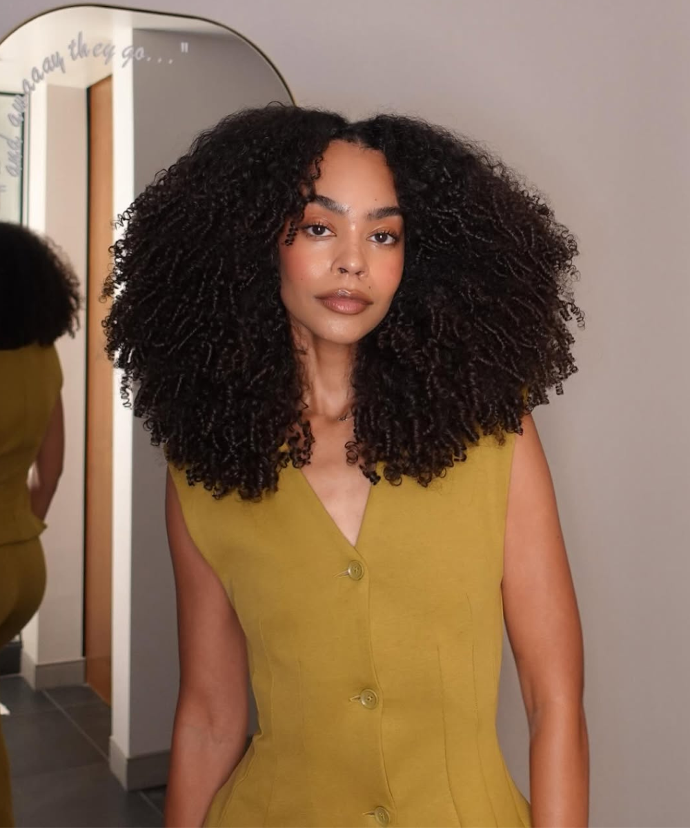 Mulher com cabelo volumoso usando um colete amarelo depois de um cronograma capilar para cabelo crespo bem feito