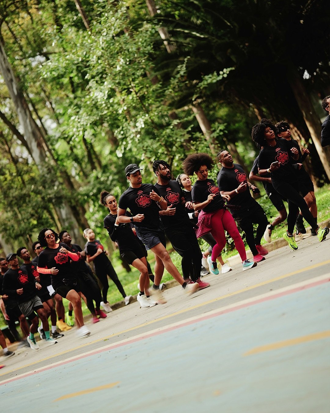 Pessoas correm em grupo em parque arborizado, promovendo a cultura da corrida.